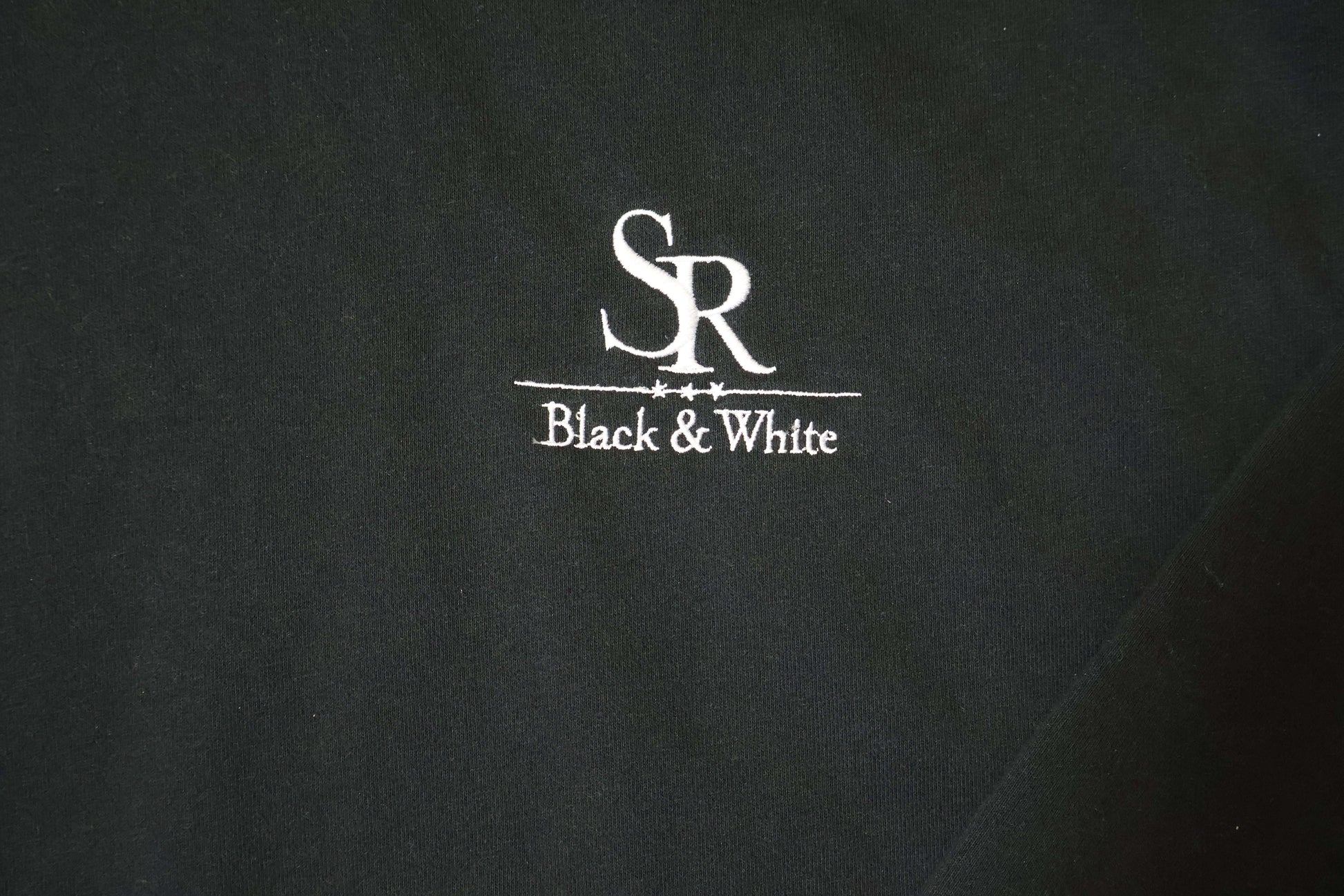 Embroidered SR Black & White logo on black fabric, showcasing the premium quality of the SR Black & White Premium Hoodie 450g - Unisex.