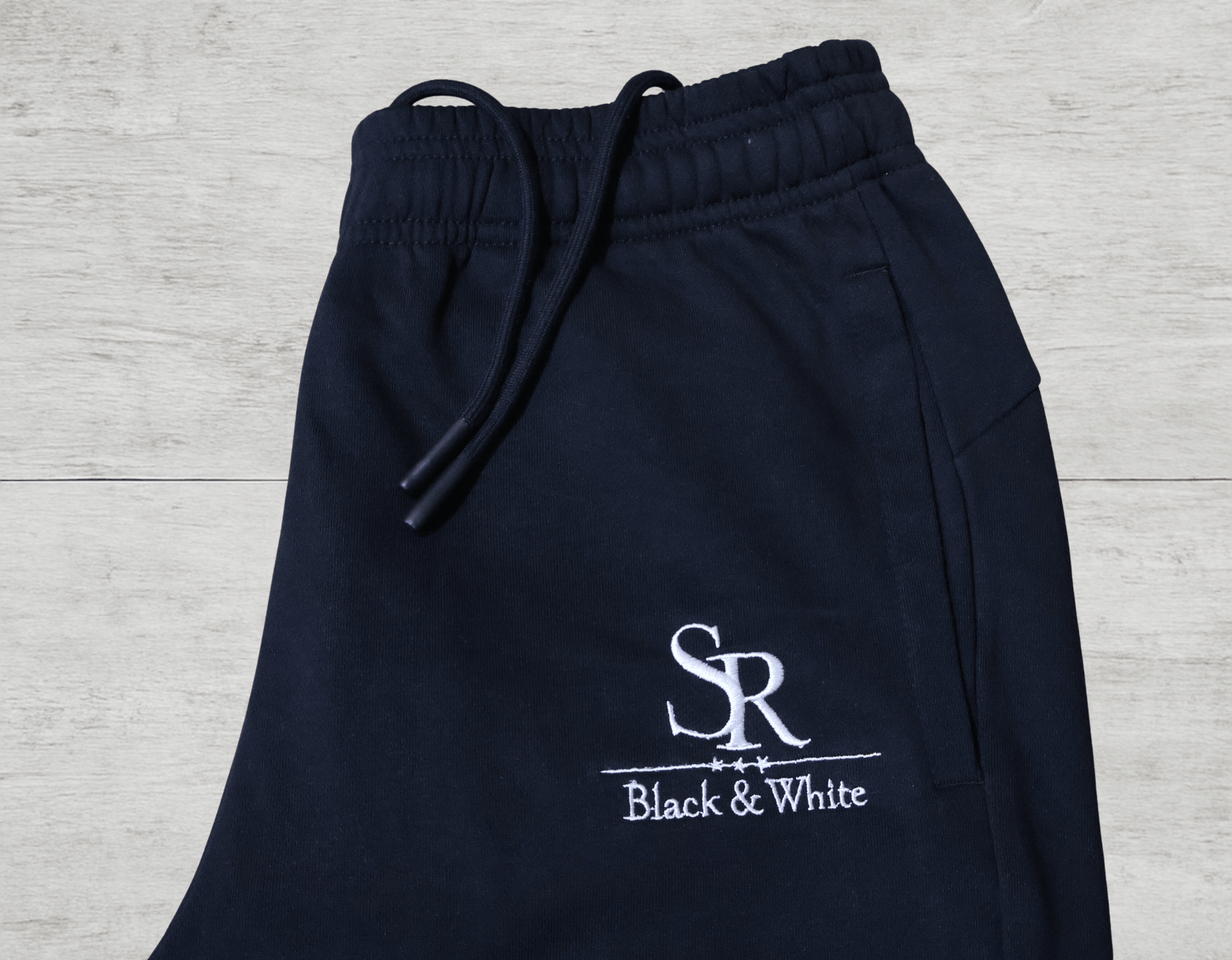 Close-up of SR Black & White Black Tracksuit – Unisex jogger pants featuring premium embroidered logo on black cotton fabric.